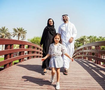 Happy young traditional family in Dubai, UAE at the park. The little girl running in front of their parents in a beautiful sunny day.